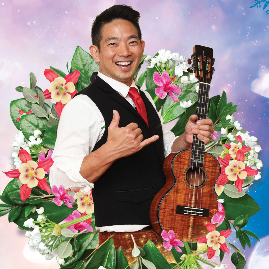 Jake Shimabukuro holds his ukulele and stands surrounded by a wreath of tropical flowers